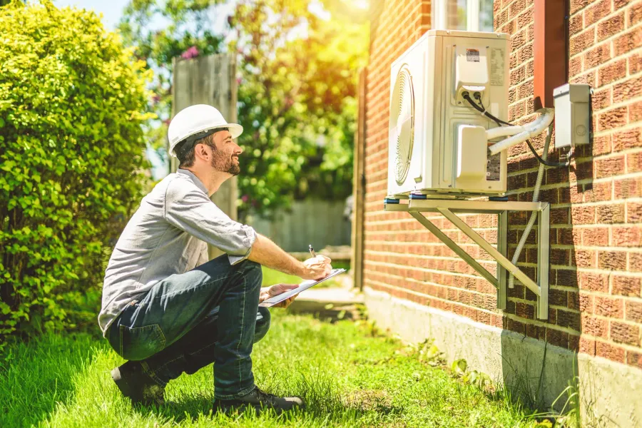 A technician inspecting an outdoor heat pump unit